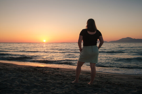 A woman standing on a beach on the island of Kos, watching the sunset.