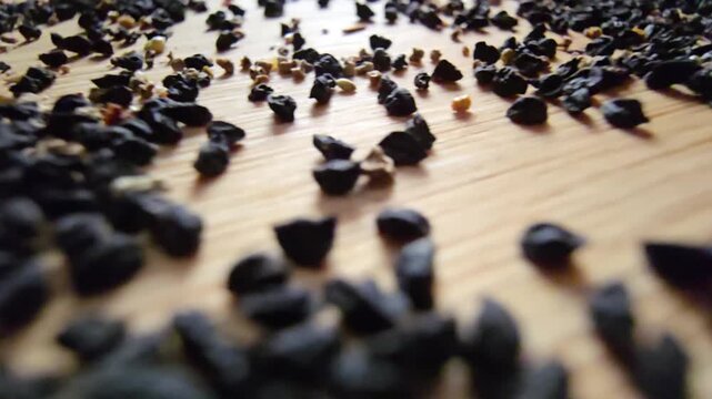 Macro close-up video of organic leek seeds scattered across a wooden surface, highlighting agricultural harvesting, gardening concepts, and healthy plant-based ingredients in a natural setting.   