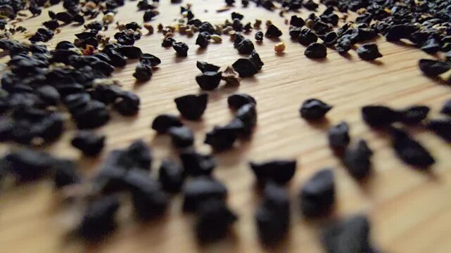 Macro close-up video of organic leek seeds scattered across a wooden surface, highlighting agricultural harvesting, gardening concepts, and healthy plant-based ingredients in a natural setting.   