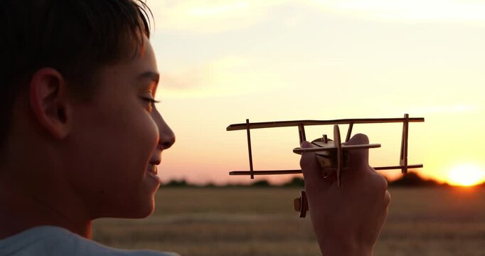 Boy holds toy airplane at sunset. Child imagines flight over golden field. Warm rural landscape creates soft nostalgic evening mood. Childhood dreams inspire adventure and creativity.