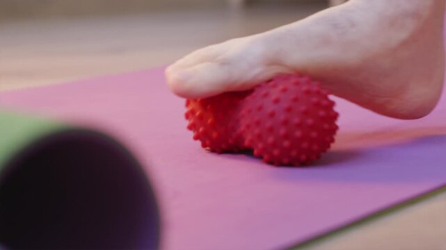Close up of foot rolling red spiky massage ball on exercise mat