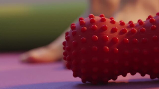 Red spiky massage ball lying on mat with foot warm up in background