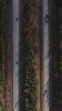 Drone footage, top down view of cars and trucks driving on a straight highway cutting through conifer forest in the Ural region, Russia, sunny day
