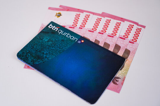 Makassar, Indonesia, September 20, A BTN Qurban iB sharia savings book placed diagonally over a neatly fanned-out stack of Indonesian 100.000 rupiah banknotes.