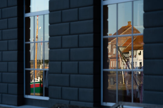 Horizontal detailed view of dark wall windows reflecting bright yellow and red historic harbour buildings under a deep blue sky.
