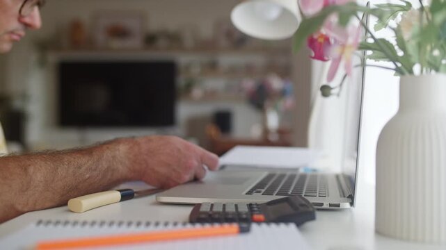 Frustrated man managing finances at his home office desk, checking bills and receipts while calculating expenses on a laptop, feeling the pressure of budget problems and economic crisis