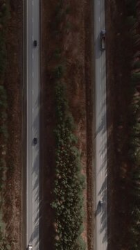 Drone top-down footage of cars and trucks driving on a straight highway between taiga forest in the Ural region, Russia, showing transport, travel and nature