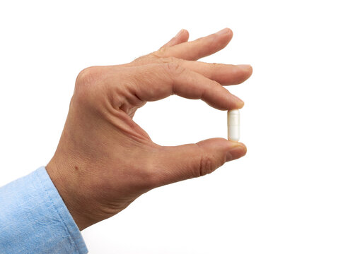 Close-up of a hand holding a white capsule against a clean white background, representing medicine, healthcare, pharmaceuticals, treatment, and medication concepts
