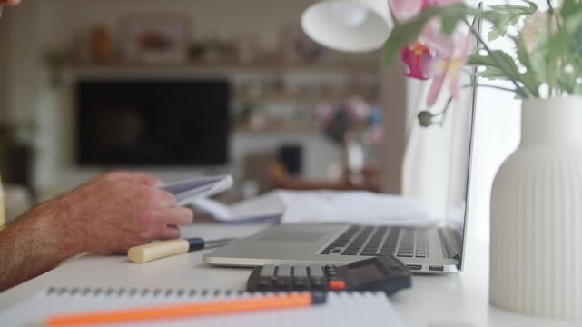Unrecognizable man sitting at a desk in his living room managing household finances, calculating expenses on a laptop, and paying bills online for tax purposes and budget planning
