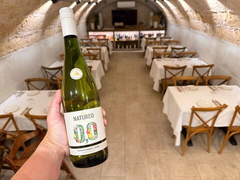 Mallorca, spain, septiembre 18, 2026 hand holding natureo 0.0 torres non alcoholic chardonnay bottle in a vacant restaurant with arched stone walls