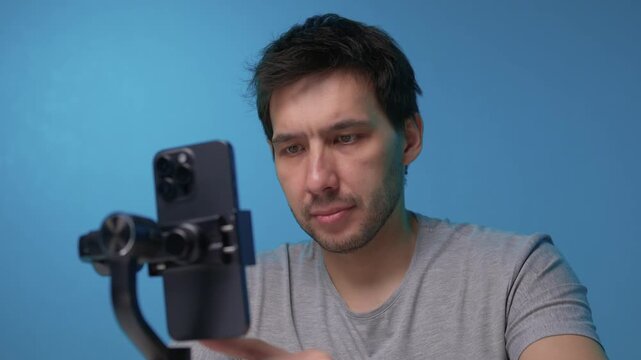 Person adjusts camera stabilizer while smiling in professional studio setup. Person in casual attire is testing camera movement techniques in blue studio environment