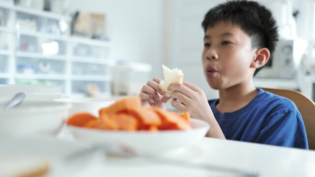 Picky Young Asian Boy Choosing Bread Over Fresh Papaya Fruit at Meal Time