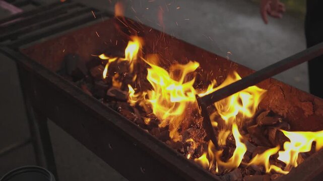 Blacksmith forge flames intensify over glowing coals inside rugged metal workshop basin