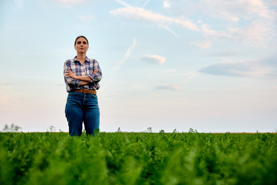 Woman farmer proudly standing with crossed arms in a vibrant green crop field, looking determined under a blue sky