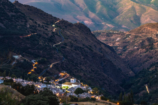 Spectacular view of Bubion set against the mountains at dawn, with car lights and the city lights (Granada, Andalusia, Spain)