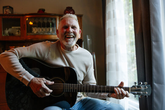 Candid senior man smiling while playing acoustic guitar at home