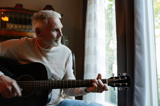 Older man playing guitar by window in a candid moment