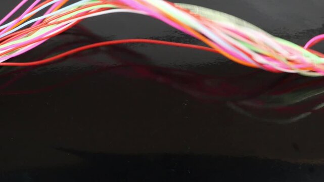 A strand of colored plastic threads sways against a glossy black background.