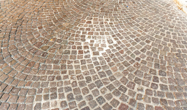 Wide view of granite cobblestone paving laid in overlapping arcs across a sunlit square with light mortar joints, classic European street surface, concept of historic urban design and stone pattern b