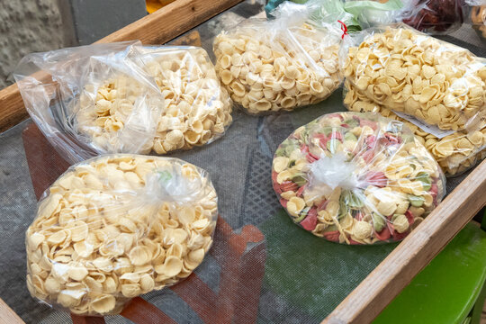 Bags of fresh handmade orecchiette pasta in plain and tricolour varieties laid out on a mesh drying screen at a street stall, concept of Italian food tradition, artisan pasta and local market shoppin
