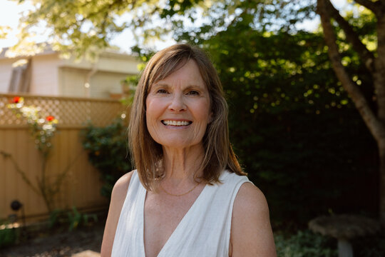 Smiling senior woman portrait in sunlit backyard, candid and hap