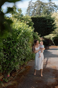 Candid grandmother helping toddler walk on sunny garden path