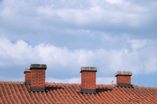 Three brick chimneys on a rooftop with cloudy sky