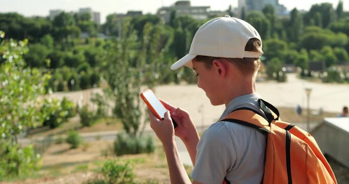 Young boy checking smartphone while sitting on city bench with backpack. Urban scene focuses on digital navigation, location awareness and using mobile technology while exploring city.