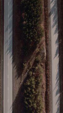 Top down drone footage of a single car traveling along an empty asphalt highway bordered by pine forest and dry vegetation in the Ural region, Russia