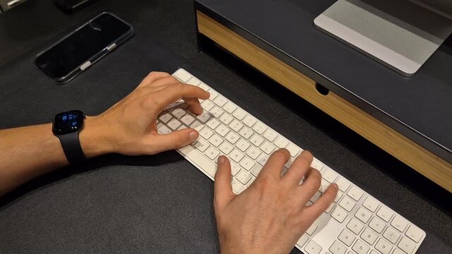 Hands typing on a white  computer keyboard at a modern workspace