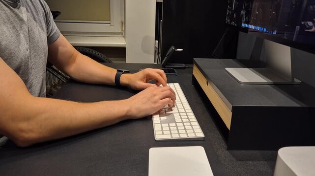 Side view of man typing on keyboard at dark desk setup with computer screen