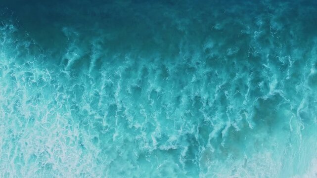 Cinematic overhead footage of ocean breakers rising, curling, and crashing into the sea, showing swirling foam, spray, and continuous water movement.