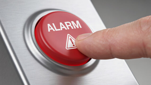 Finger pressing red alarm button on metallic control panel