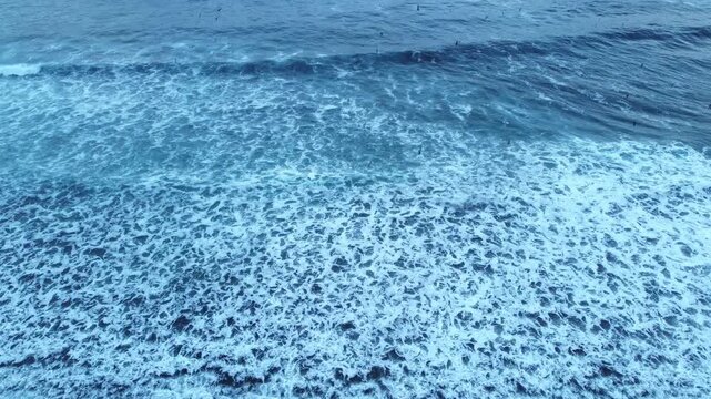 Turquoise seawater and rolling surf waves collide and spread into frothy whitewater, filmed from above as a peaceful natural seascape background.