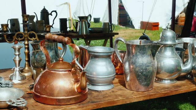 Vintage copper and pewter kitchenware displayed on wooden table at outdoor historical reenactment festival.