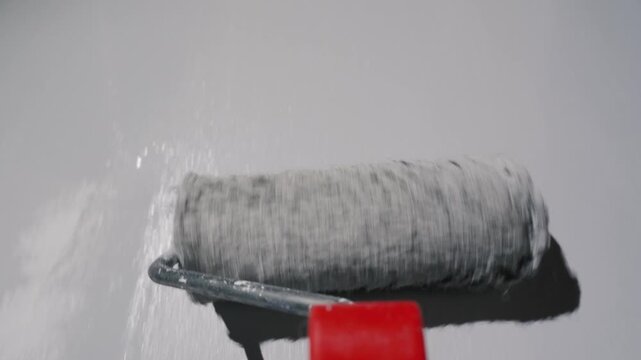 Close-up shot of a paint roller with red handle moving across white wall creating texture.