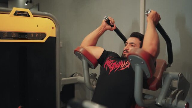 Medium close up video shot of a focused bearded man performing seated ab crunch machine exercise for core strength and abdominal muscle conditioning in a gym.