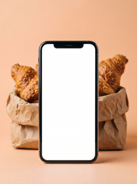 smartphone with blank screen standing in front of paper bag with fresh croissants mock up