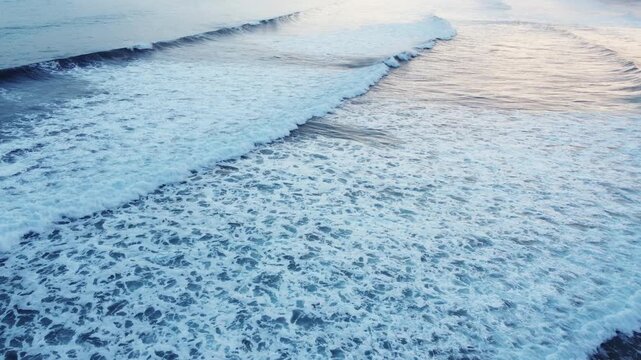 Aerial view of powerful ocean waves breaking into white foam across the open sea, creating a dynamic natural water texture with no visible land.