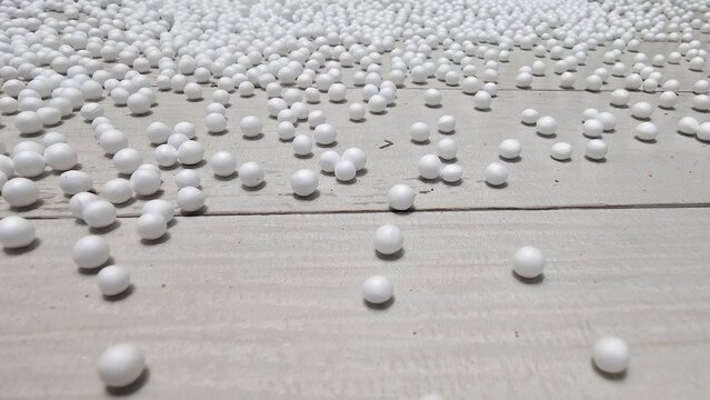 White polystyrene foam beads scattered on a wooden floor background, insulation material, copy space.
