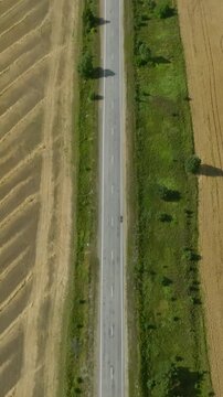 Drone footage of a rural road junction cutting through golden harvested farmland and green tree lines in the Ural region, Russia, showing summer agriculture landscape