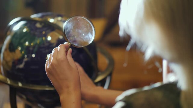 Young person's hands holding magnifying glass over globe, exploring geography and world map.
