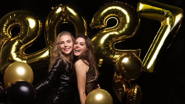 Happy gorgeous girls in stylish sexy party dresses holding gold 2027 balloons, having fun at New Year's Eve Party.