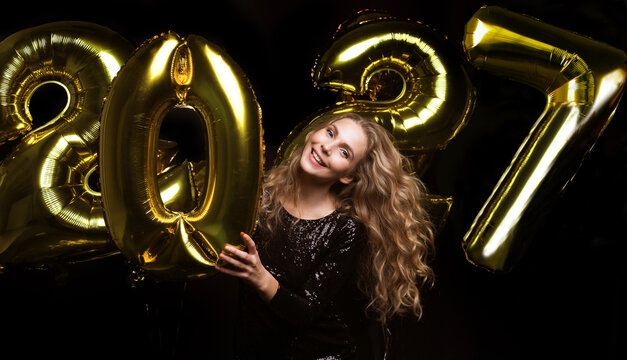 Happy gorgeous girl in stylish sexy party dress holding gold 2027 balloons, having fun at New Year's Eve Party.