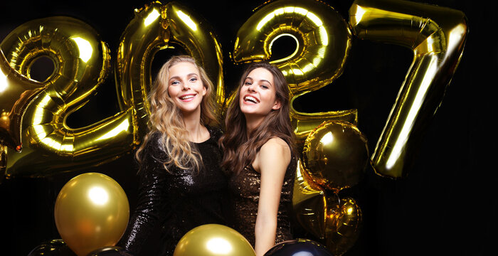 Happy gorgeous girls in stylish sexy party dresses holding gold 2027 balloons, having fun at New Year's Eve Party.