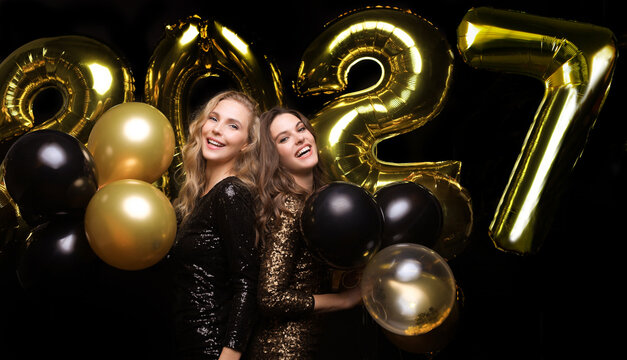 Happy gorgeous girls in stylish sexy party dresses holding gold 2027 balloons, having fun at New Year's Eve Party.