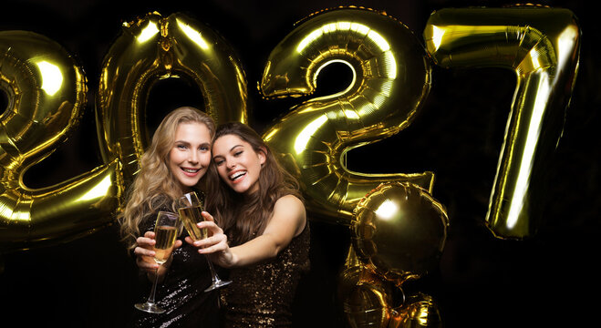 Two young ladies drinking champagne. Image of girls with balloons isolated on black background, having fun at New Year's 2027 Eve Party.