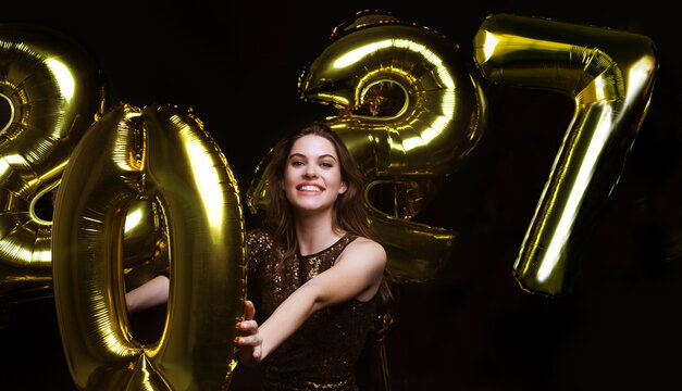 Happy gorgeous girl in stylish sexy party dress holding gold 2027 balloons, having fun at New Year's Eve Party.