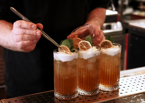 Garnishing drink. Bartender work. Man hand tweezers putting dried citrus slice in cocktail set glass with whipped top mint leaves.