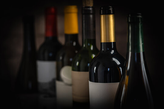 Close-up view of various wine bottles, with a glass of red wine and grapes blurred in the background, creating an elegant and sophisticated wine composition Perfect for wine-themed compositions